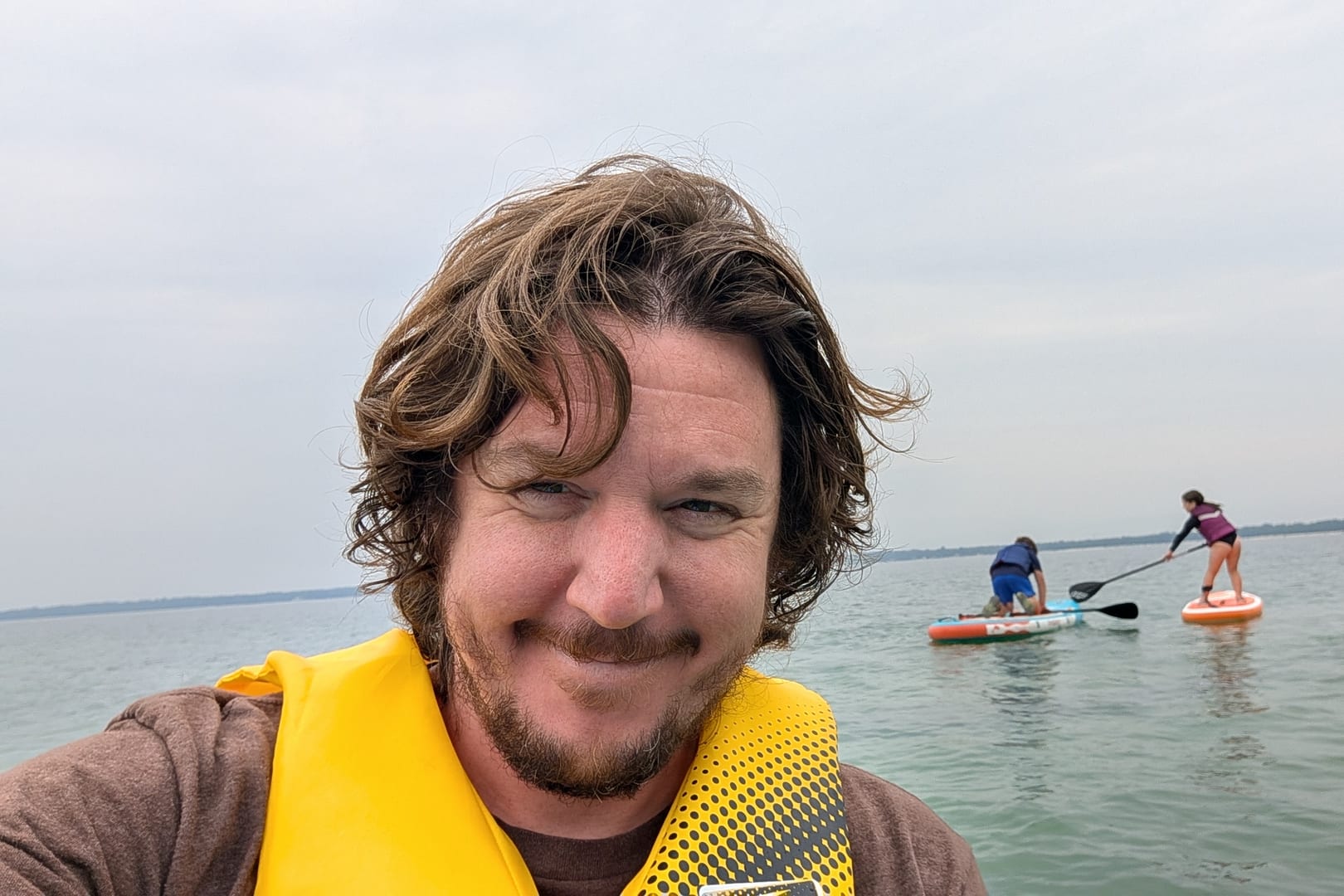 Alex Pigeon on the water, with his children paddleboarding in the background.